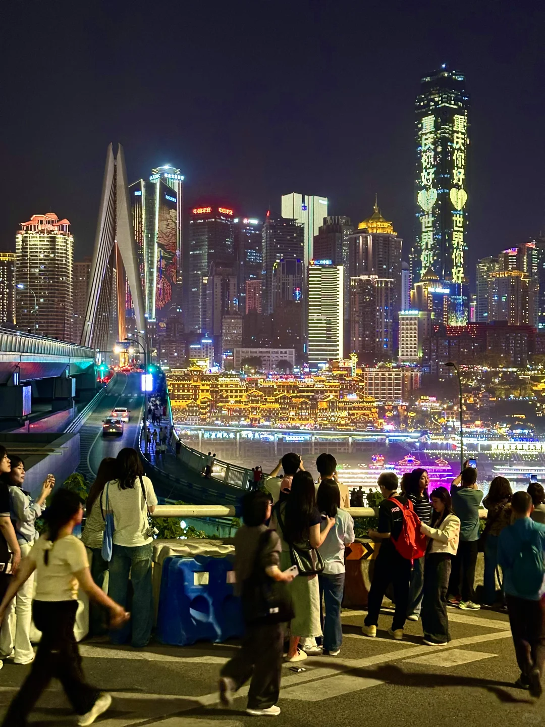 Illuminated multi-tier traditional stilt houses of Hongyadong seen from Qiansimen Bridge at night with city skyline lights.